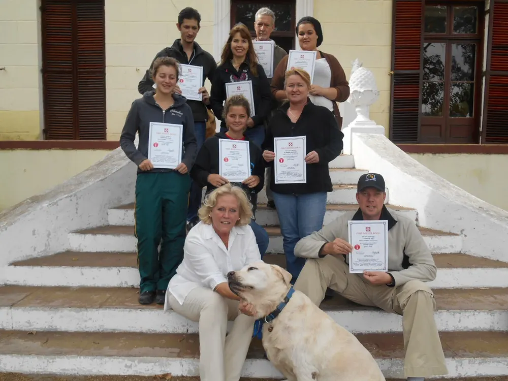 A group of pet sitters holding their training certificates on the steps of a building, with a Labrador in front